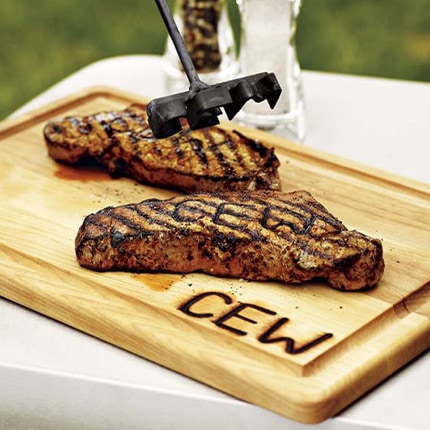 Two grilled steaks branded with CEW steak brand laying on a wooden cutting board also branded with the letters CEW.
