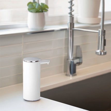 A white Simplehuman rechargeable touch-free soap dispenser on a counter next to a sink