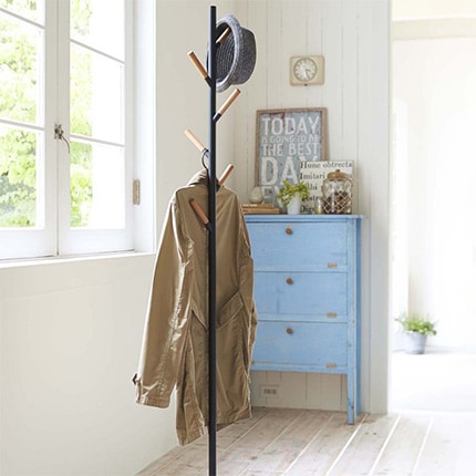 A jacket hanging from a Yamazaki Home Plain coat rack in a bedroom next to a window with a blue dresser in the background.