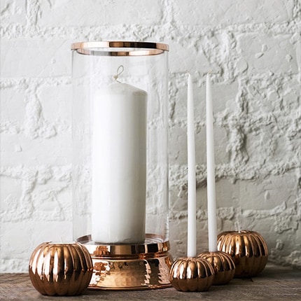 A set of white taper candles arranged on a wooden mantel in front of a white brick wall.