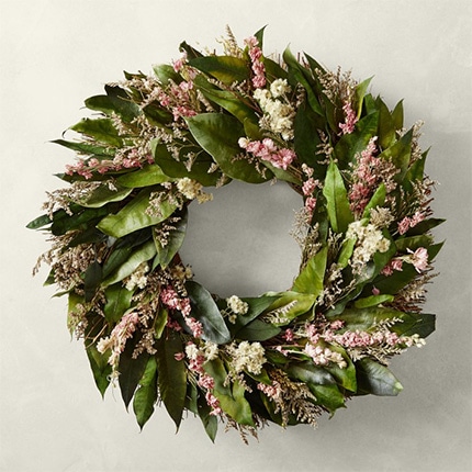 A pink larkspur any-season wreath hanging from a white wall.