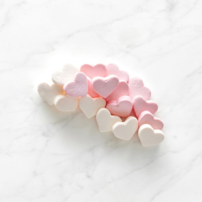 White and pink heart-shaped marshmallows are scattered from a cup