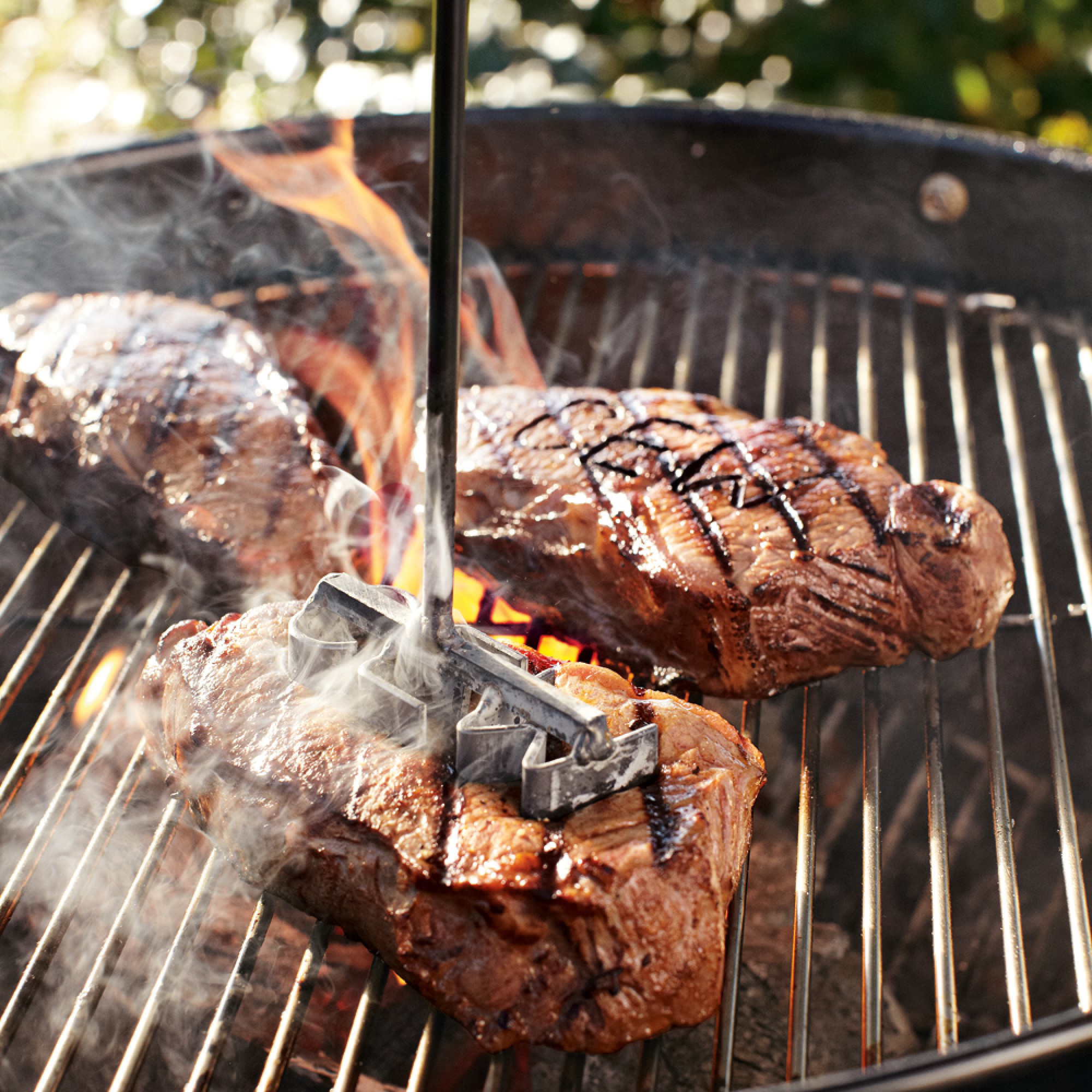 A monogrammed steak brand being used on a piece of steak on a grill