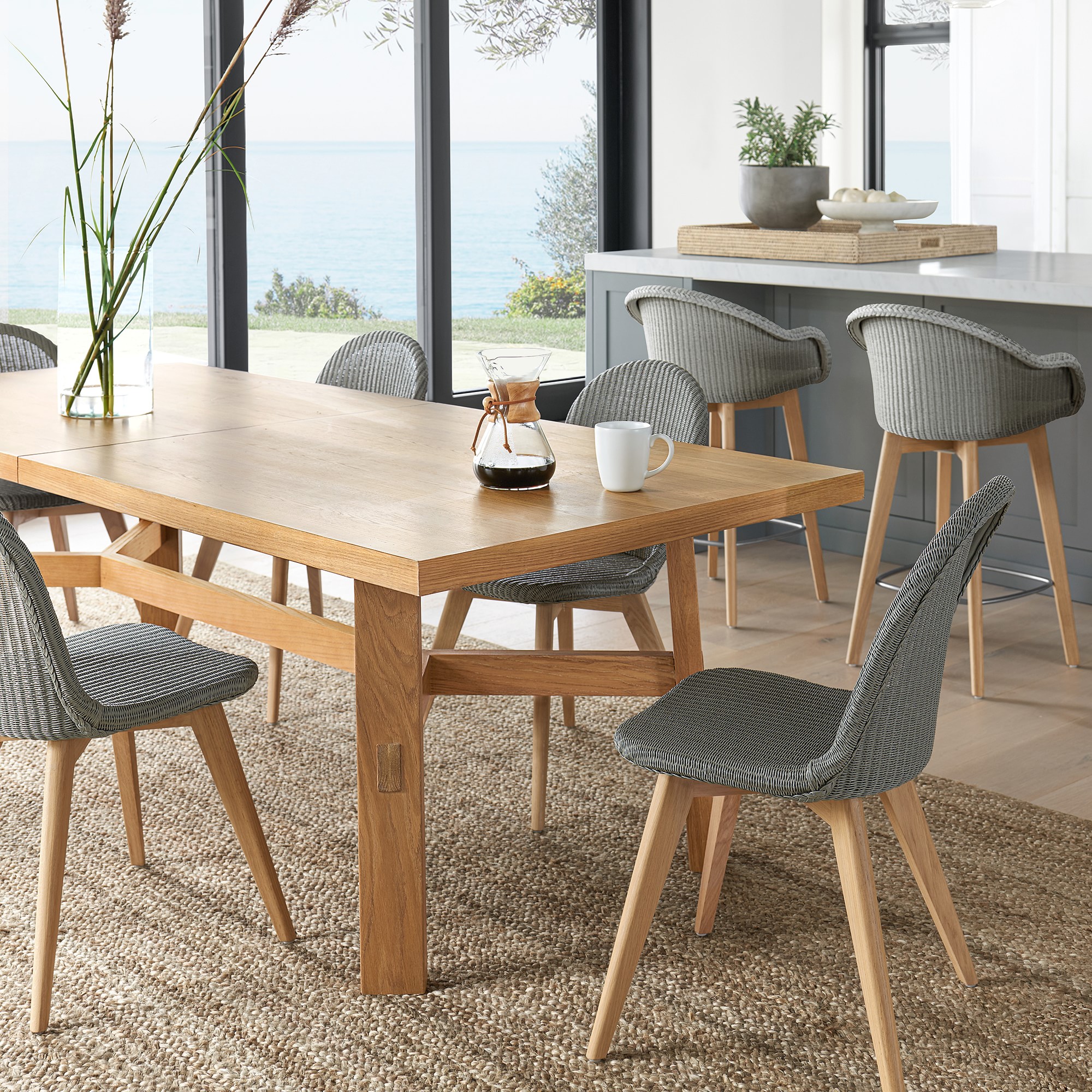 Set of grey woven chairs around a wooden dining table in a bright kitchen/dining area.