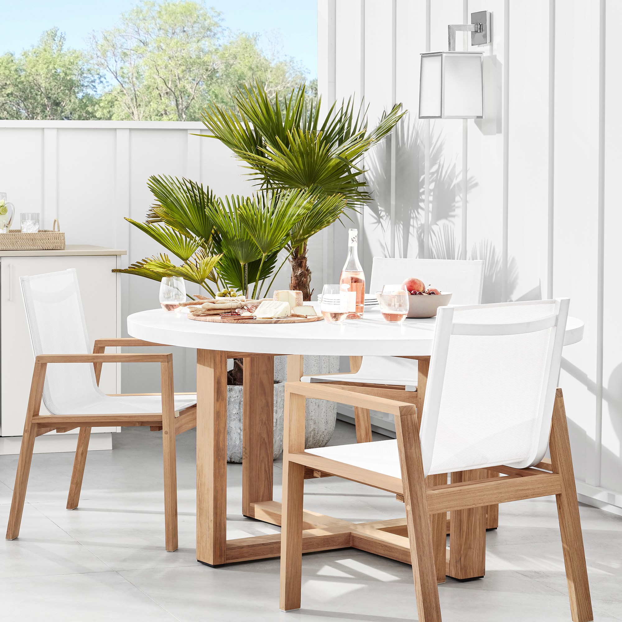 White outdoor dining chairs with wooden frames around a round table with food and drinks