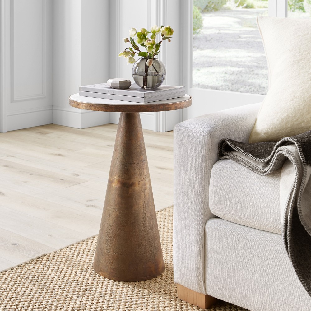 Rustic conical metal side table with round marble top, paired with neutral living room decor.