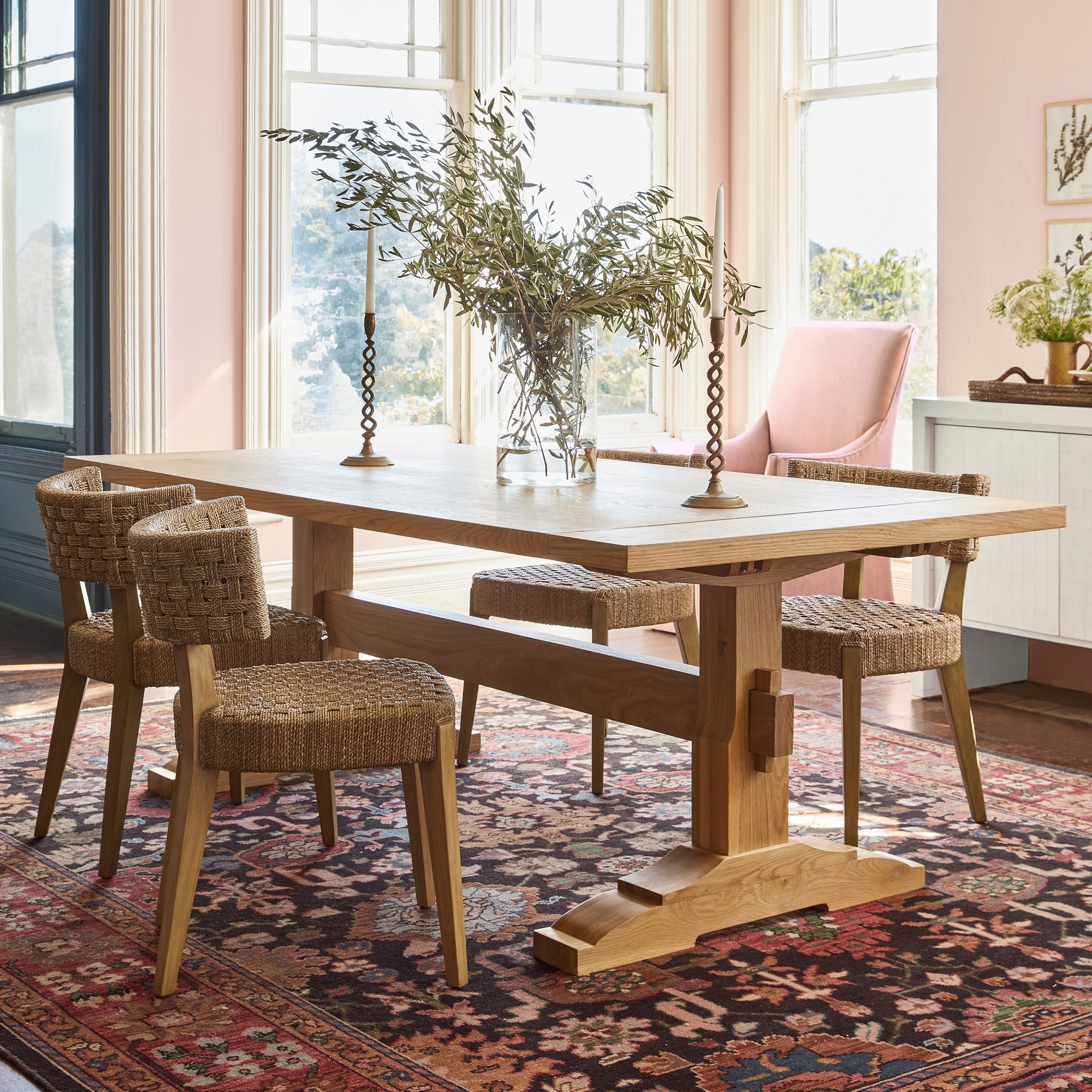 A large wooden dining table with woven chairs around it in a bright, elegant dining room.