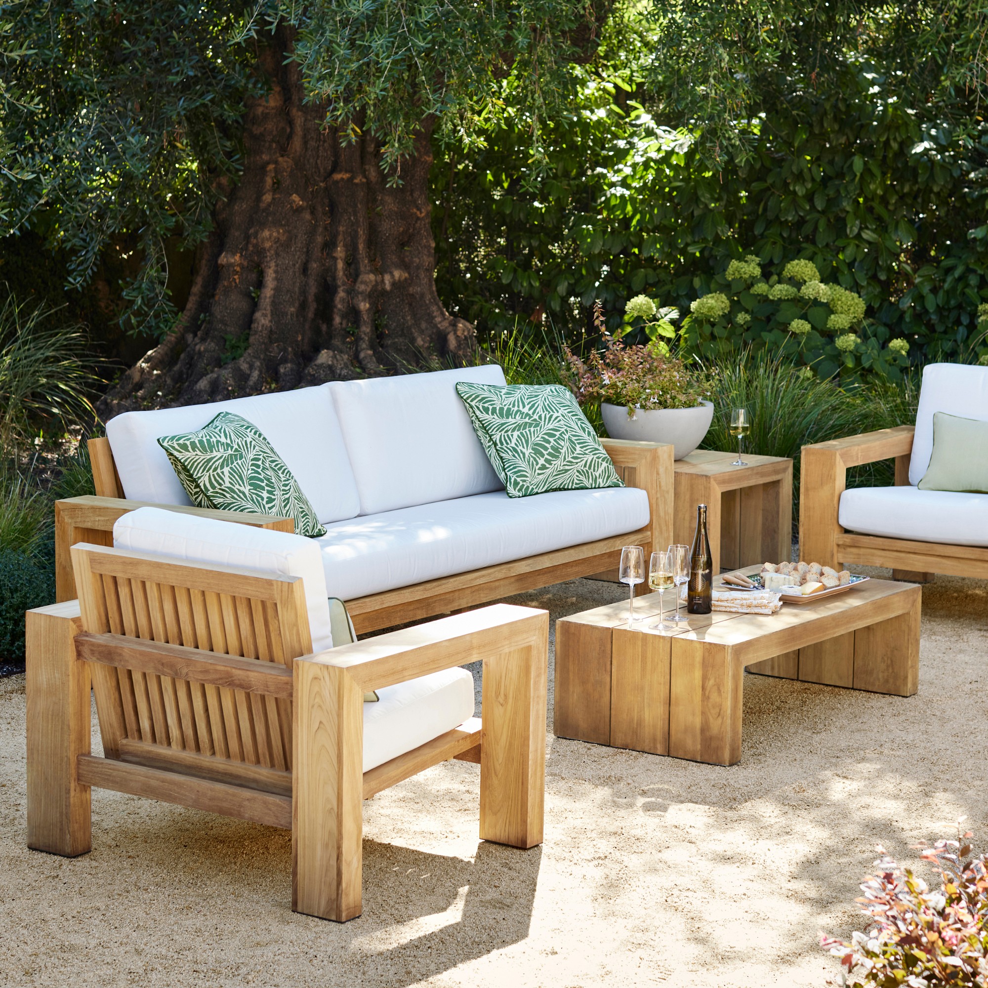 Set of outdoor furniture with white cushions and green patterned throw pillows on a patio