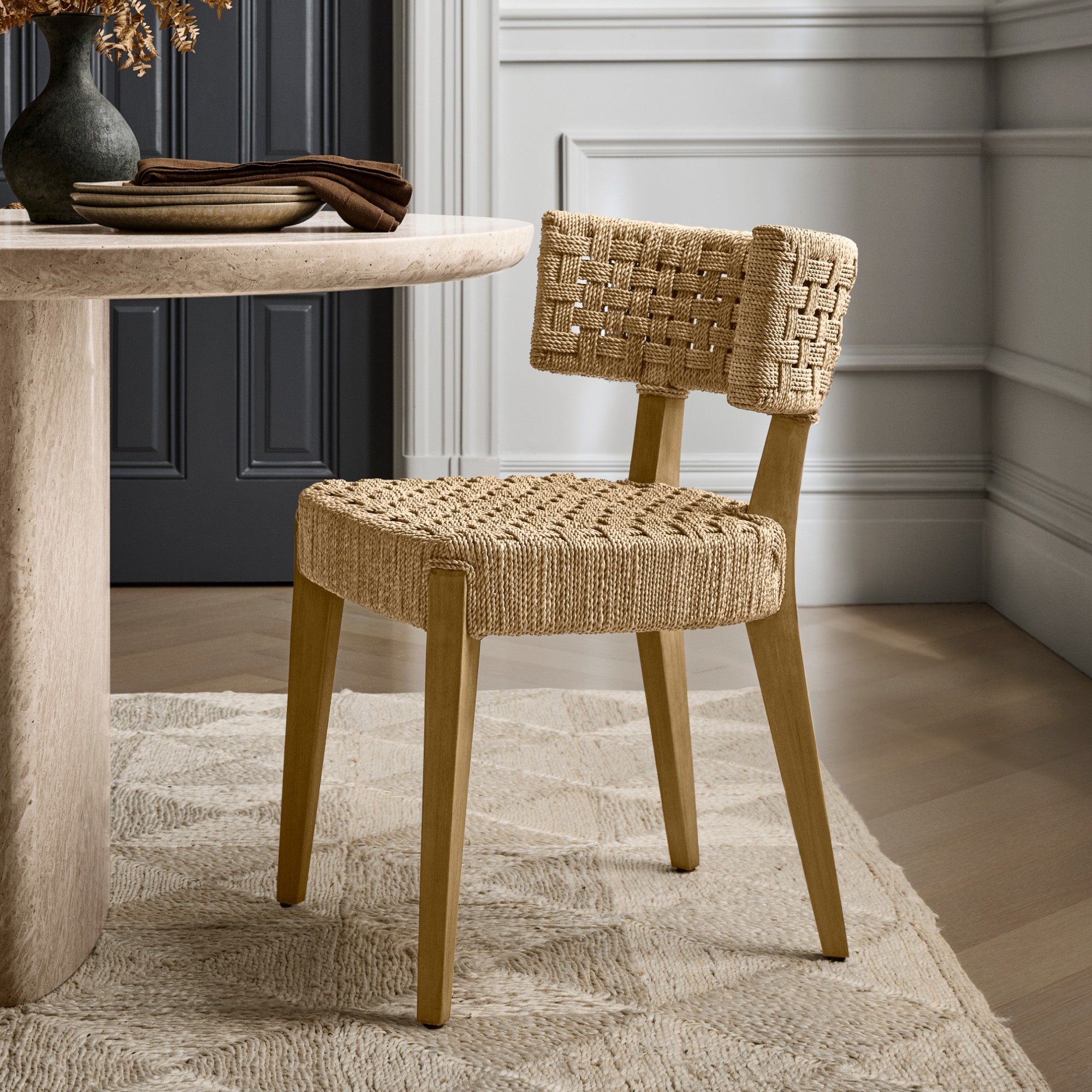 A woven natural fiber chair with wooden legs placed beside a round table in a bright dining room.