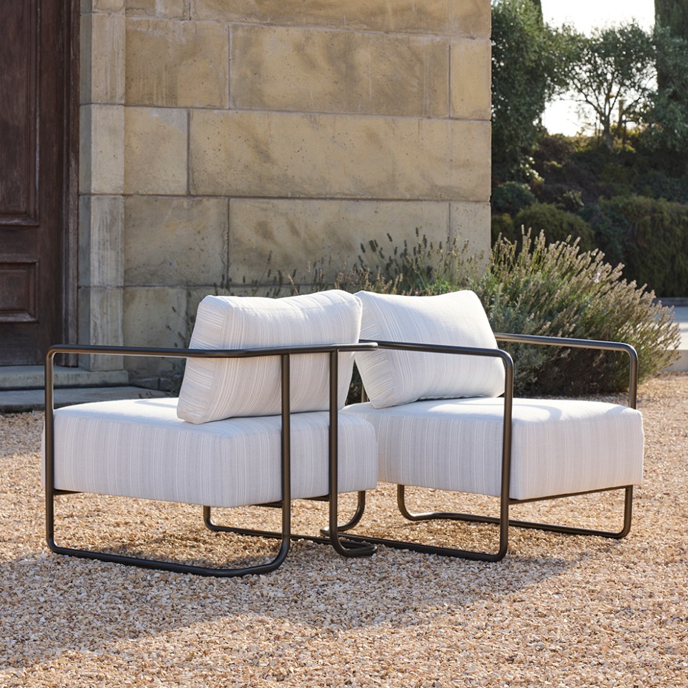 Two outdoor upholstered chairs with white cushions and matching pillows arranged together